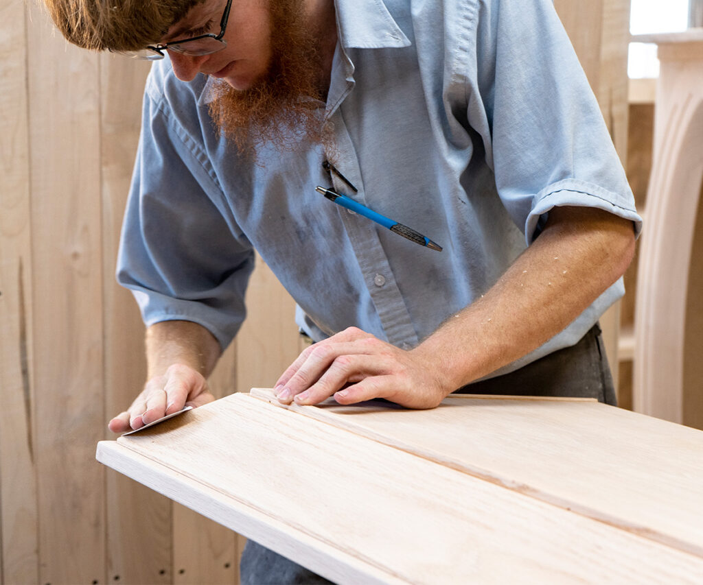 Amish craftsman inspecting solid-wood panel—handcrafted furniture with no mass-production shortcuts.