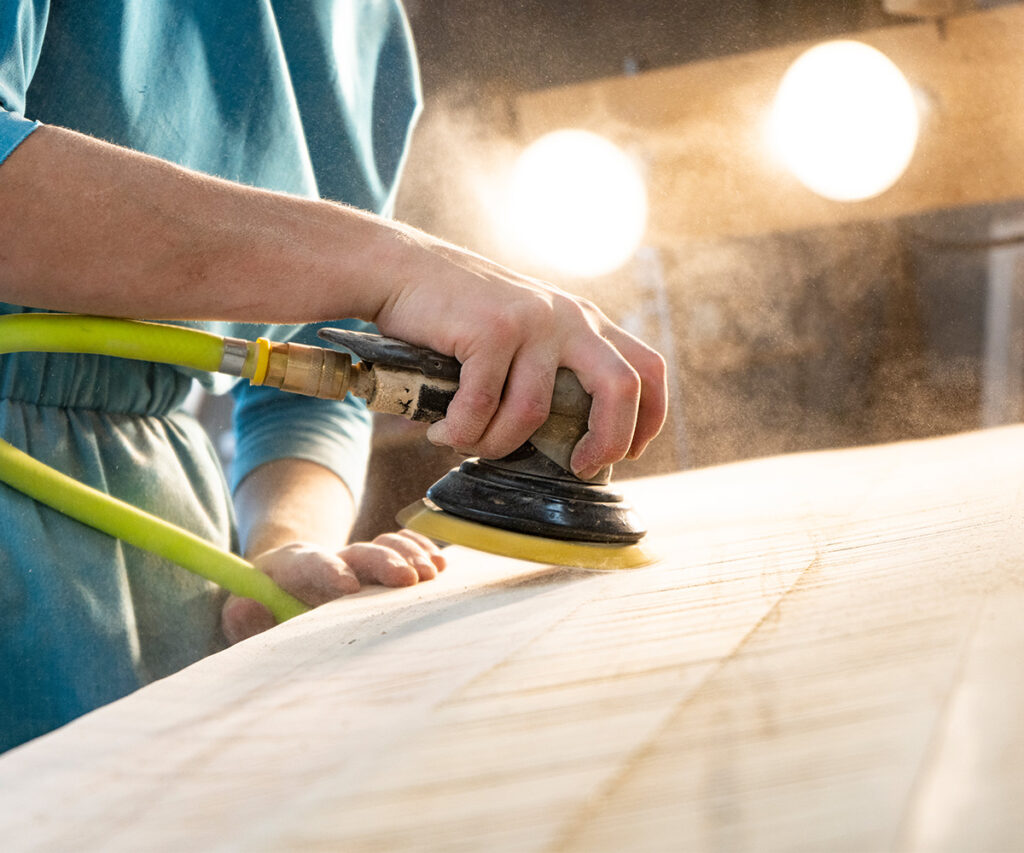 Artisan hand-sanding solid wood tabletop, achieving smooth finish on Amish crafted furniture.