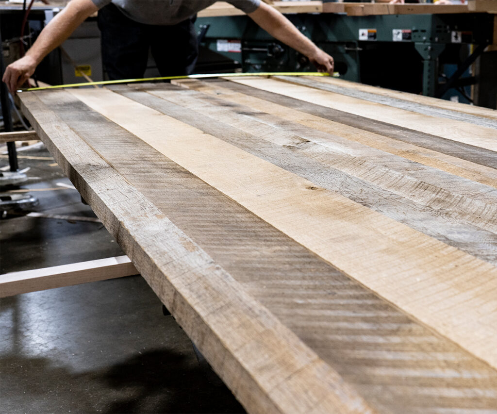 Woodworker measuring rough-sawn hardwood tabletop in workshop, showcasing Amish furniture craftsmanship and superior materials.