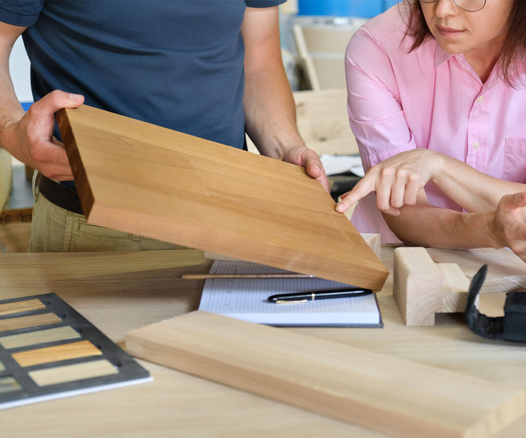 Two people reviewing a wood sample and design details at a worktable.