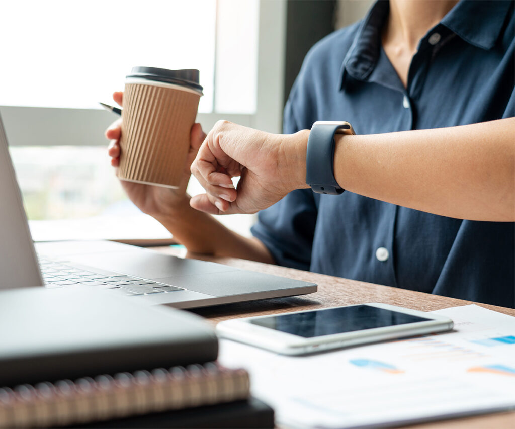 Person checking a smartwatch while holding coffee at a desk.
