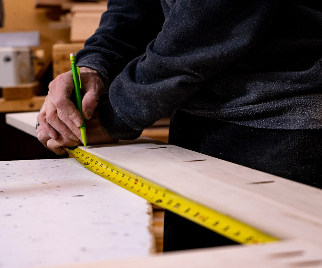 Person marking a wood board while measuring it with a tape measure.